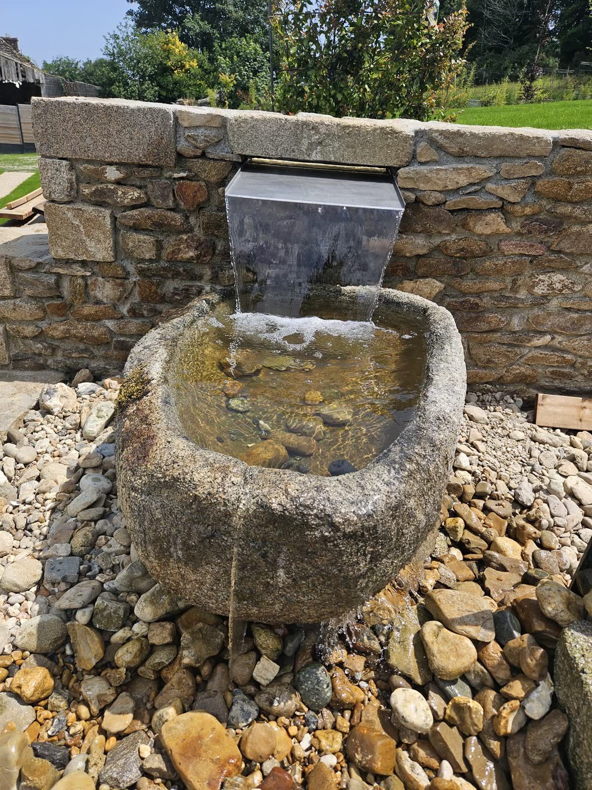 Lame d’eau inox tombant dans une auge ronde en granit posée sur des galets — Guipavas