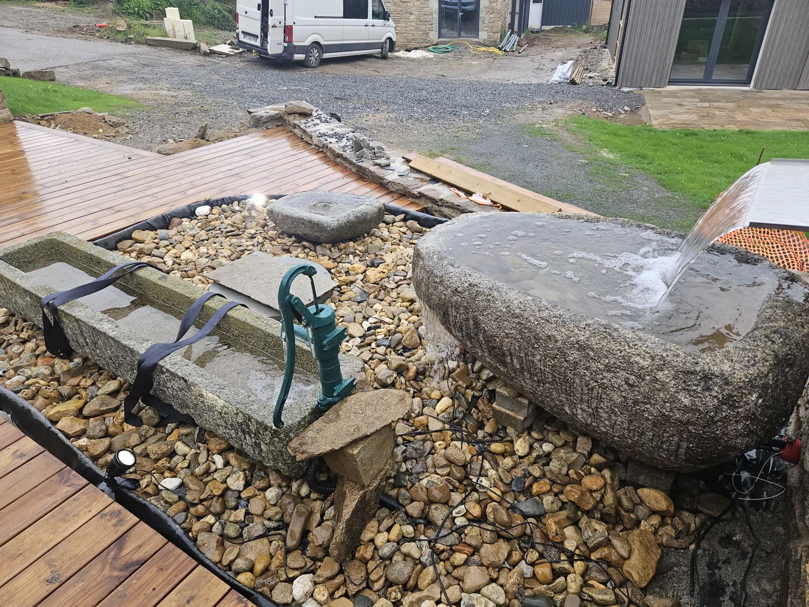 Pendant le chantier: les auges sur les galets, une pompe à bras en fonte verte posée dans l’une d’elles, gravats et bâche autour