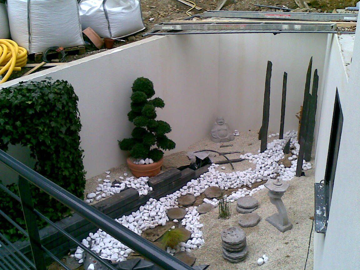 Le patio japonais: gravier clair, ruisseau de galets blancs, pieux de schiste dressés et arbre nuage