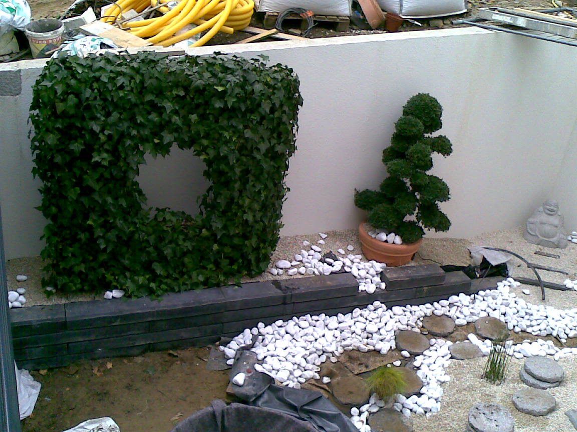 Un cube de lierre taillé, percé d’une fenêtre carrée, habille le mur aveugle; à côté un arbre nuage en pot et le lit de galets blancs