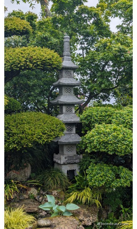 Pagode de granit à cinq étages, élancée, entre des arbustes taillés en nuage et un lit de pierres planté d’hostas
