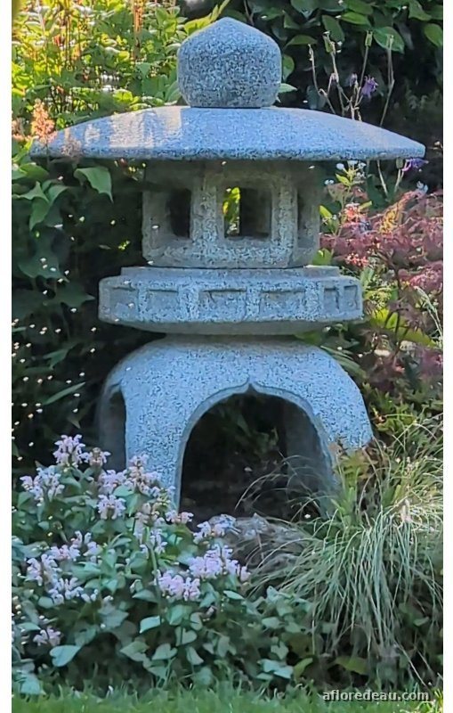 Lanterne Sennyuji gris-bleu: large chapeau surmonté d’une boule, grande ouverture en arc à la base, dans un massif d’hostas et de fleurs mauves