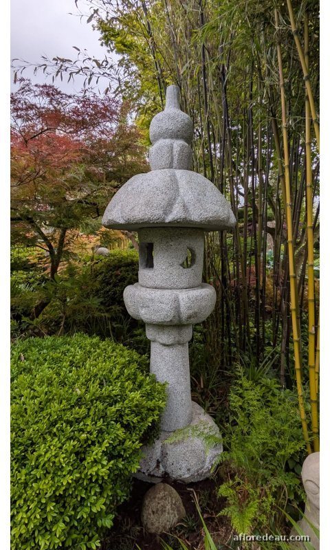 Lanterne Yoshino: une haute lanterne de granit clair sur sa colonne, chapeau à pans, dressée devant des bambous dorés et un érable qui rougit