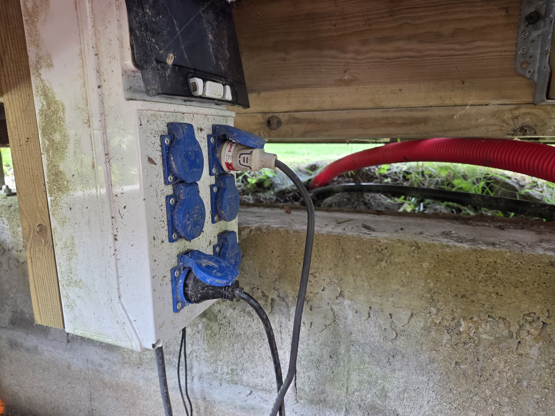Un coffret de prises étanches fixé sous un plancher bois, la gaine rouge et les câbles qui filent vers le local